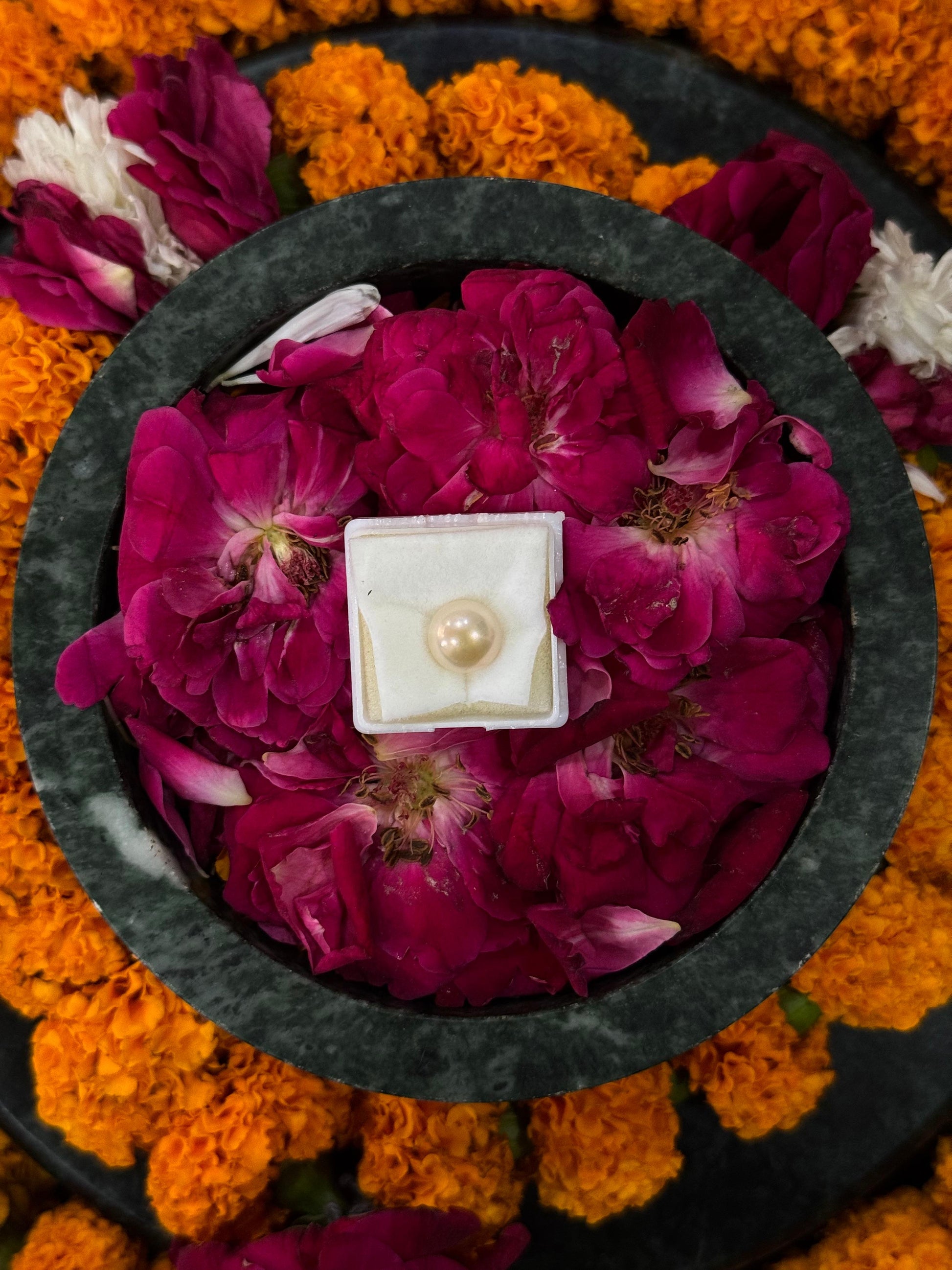 Pearl necklace in a box on pink flowers surrounded by orange and white flowers