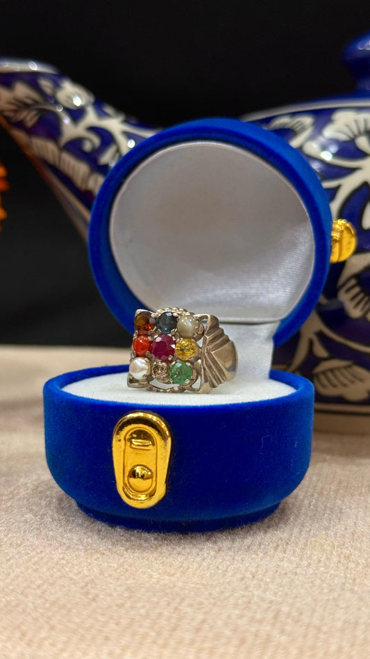 Ring with colorful gemstones in a blue jewelry box on a textured surface.