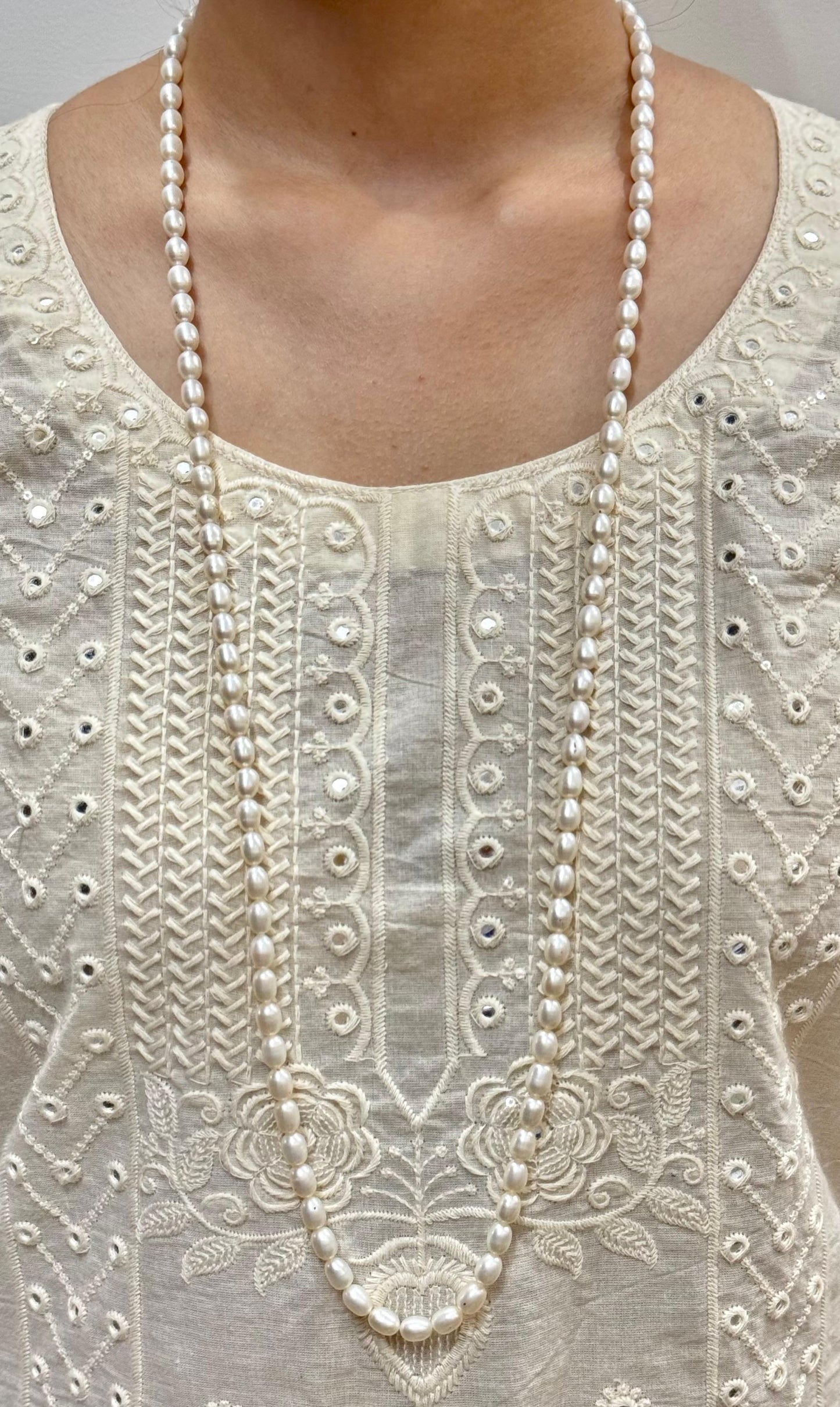 Close-up of a white embroidered garment with a long pearl necklace.