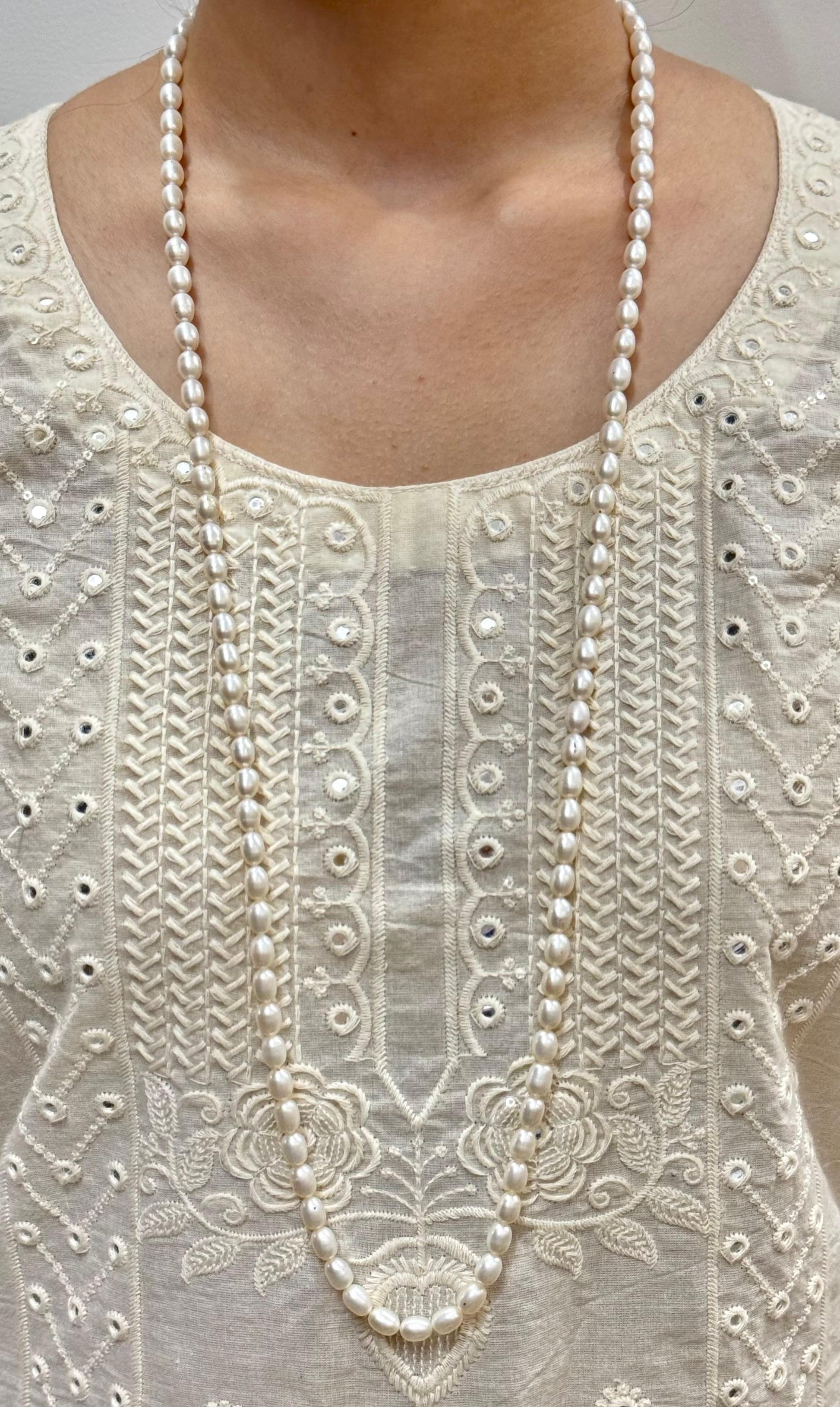 Close-up of a white embroidered garment with a long pearl necklace.