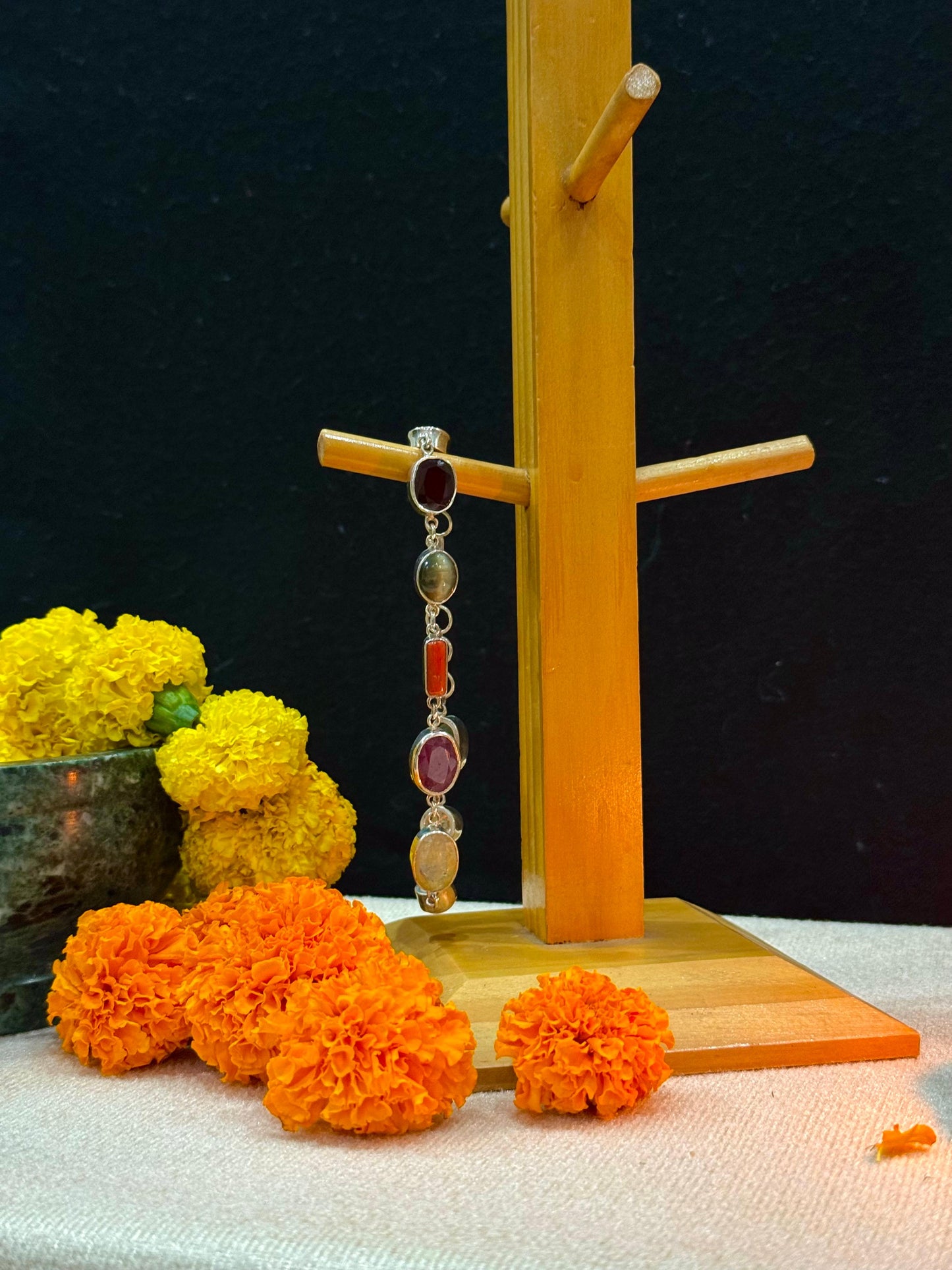 Jewelry stand with a bracelet, surrounded by marigold flowers on a dark background