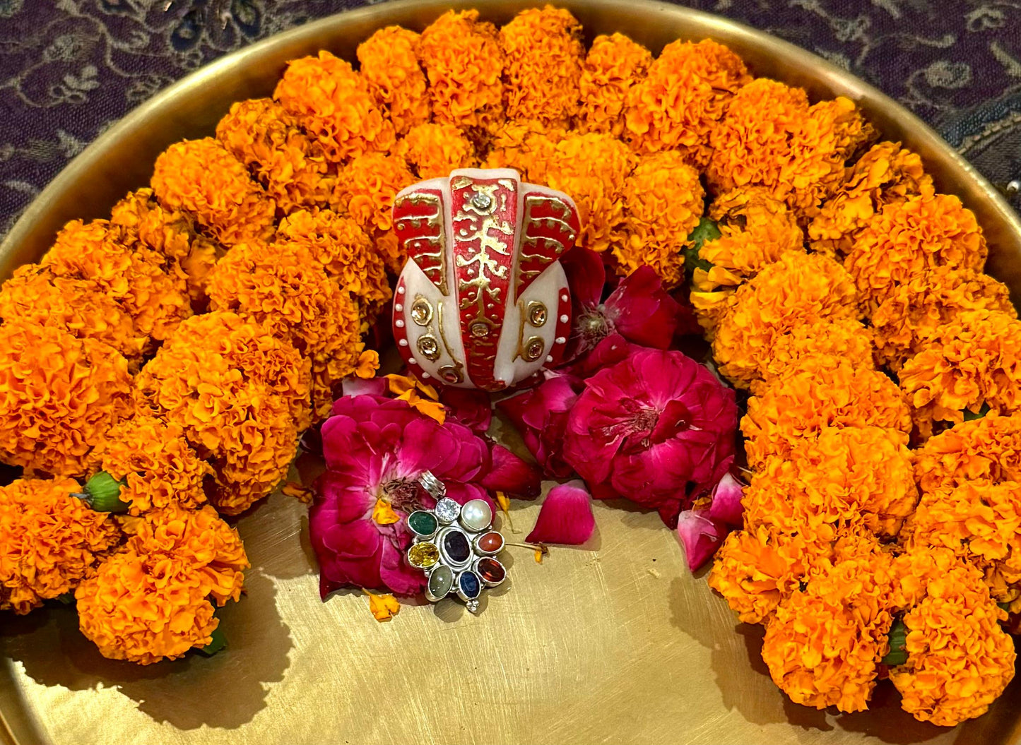 Decorative arrangement of orange marigold flowers and pink flowers with a central red and white object on a gold tray.