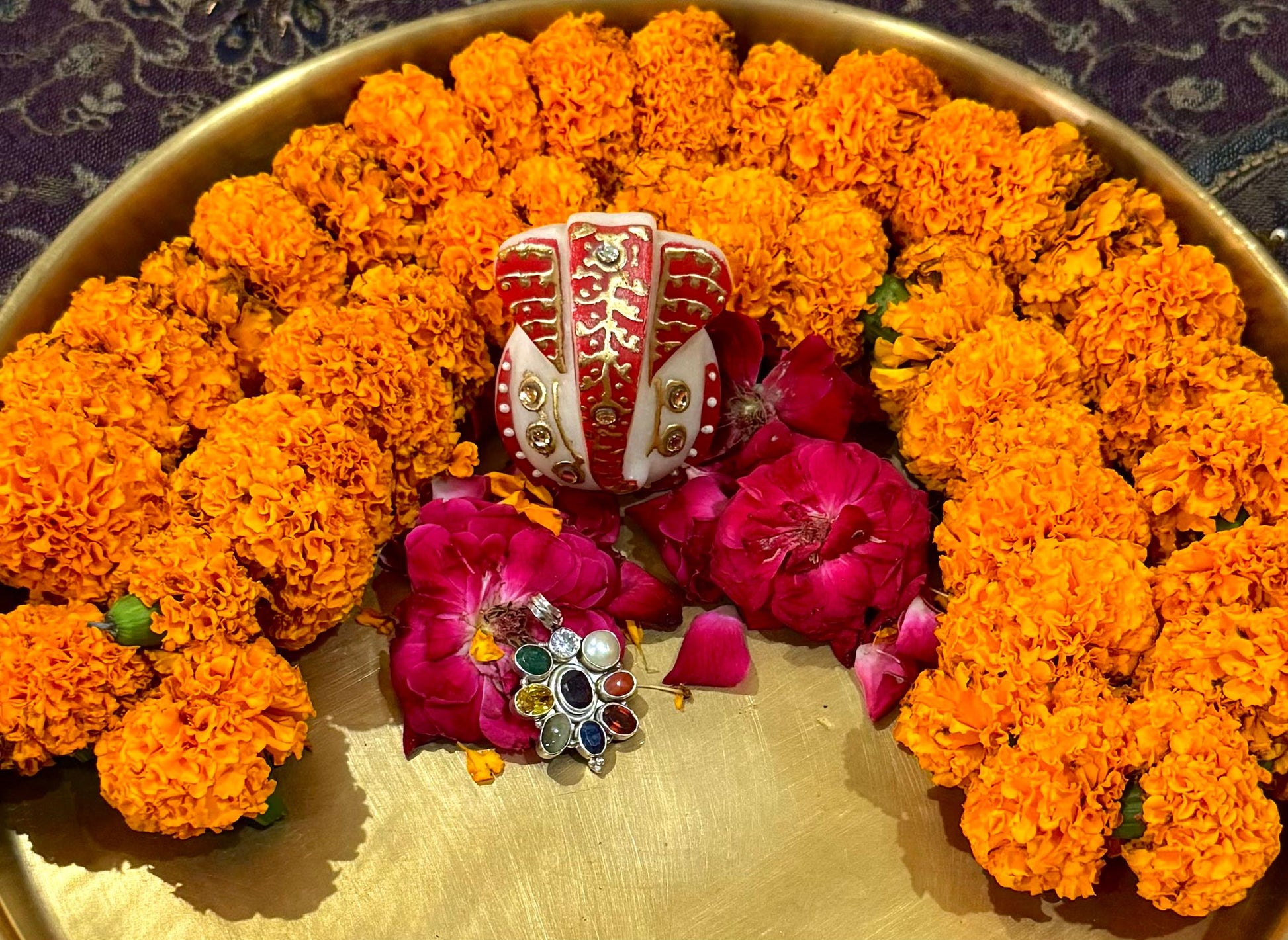 Decorative arrangement of orange marigold flowers and pink flowers with a central red and white object on a gold tray.