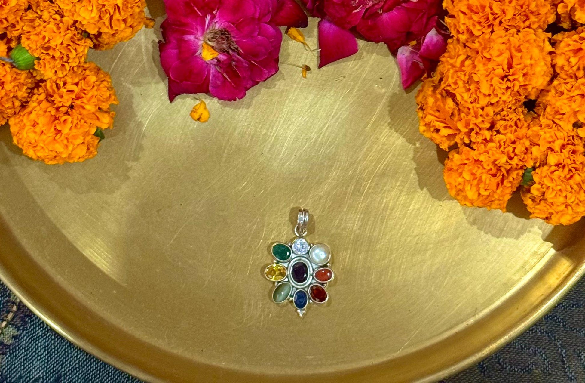 Multicolored gemstone pendant on a gold plate with marigold flowers