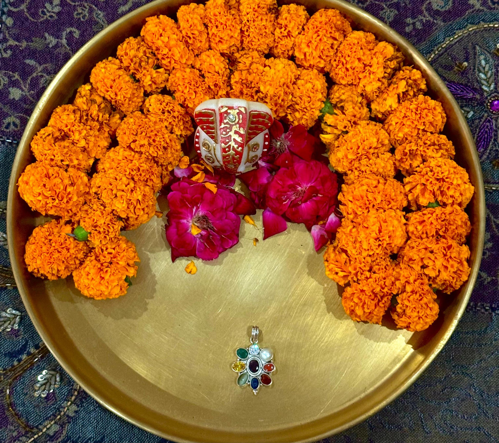 Decorative arrangement of orange marigold flowers and pink roses on a gold plate with a colorful pendant.