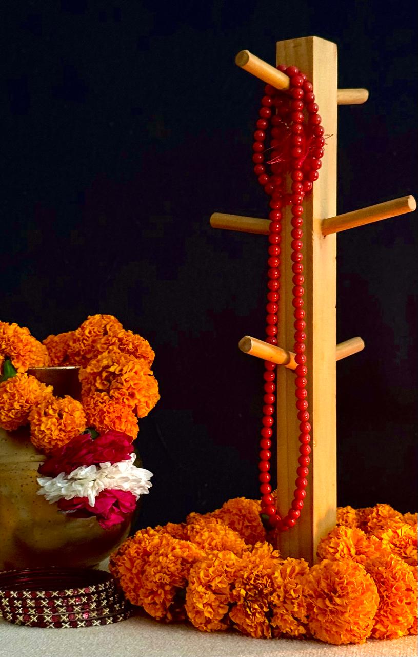 Red beaded necklace on a wooden stand with marigold garlands and a dark background