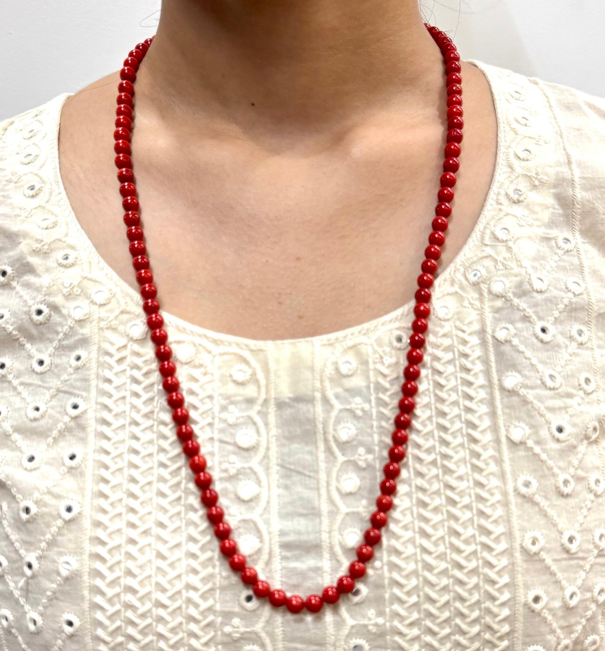 Red beaded necklace worn by a person on a white textured background