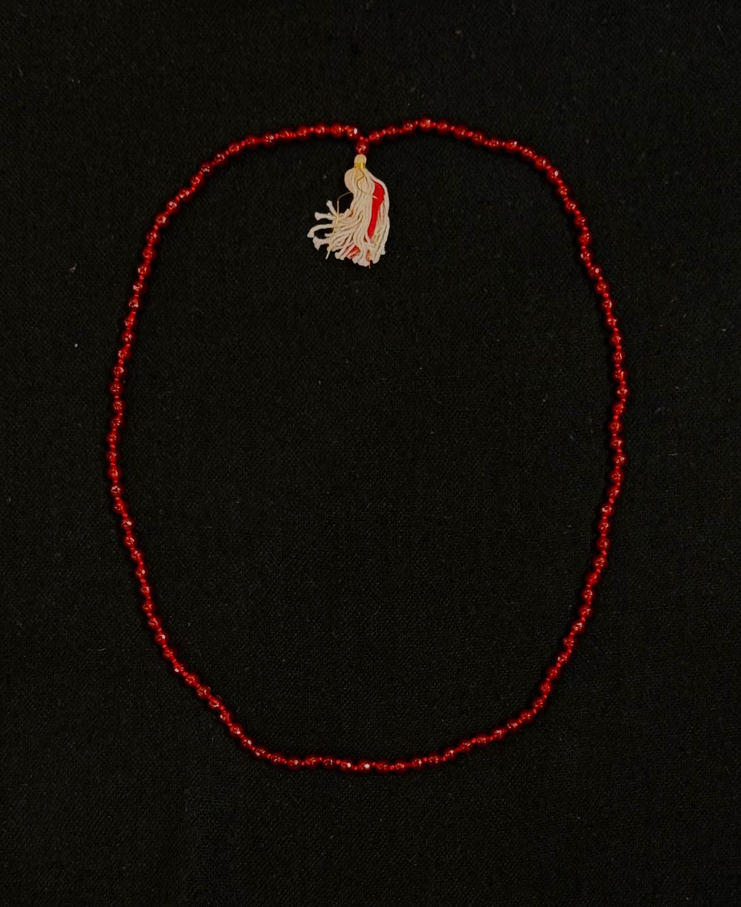 Red beaded necklace with a small embroidered pendant on a black background