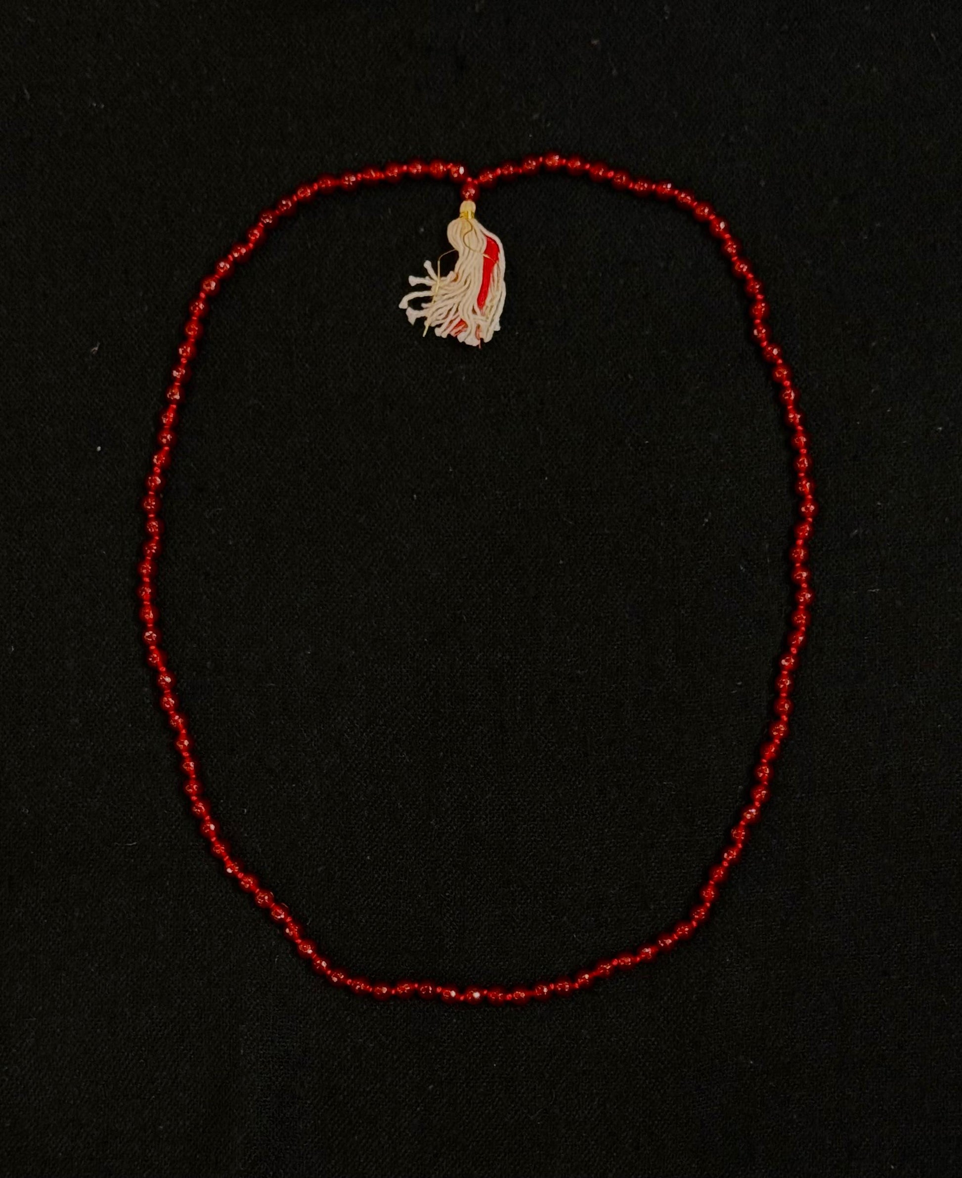 Red beaded necklace with a small embroidered pendant on a black background