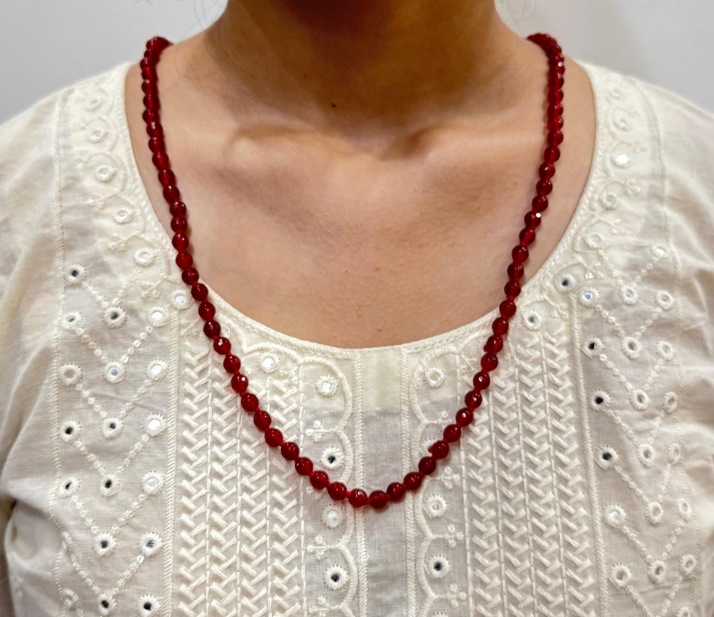 Red beaded necklace worn by a person on a white embroidered top