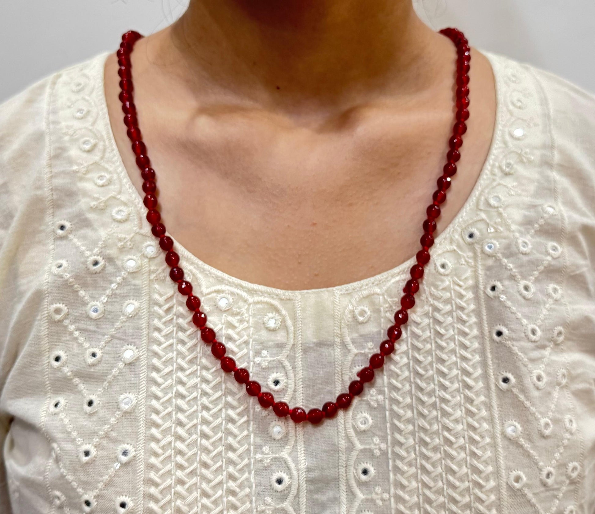 Red beaded necklace worn by a person on a white embroidered top