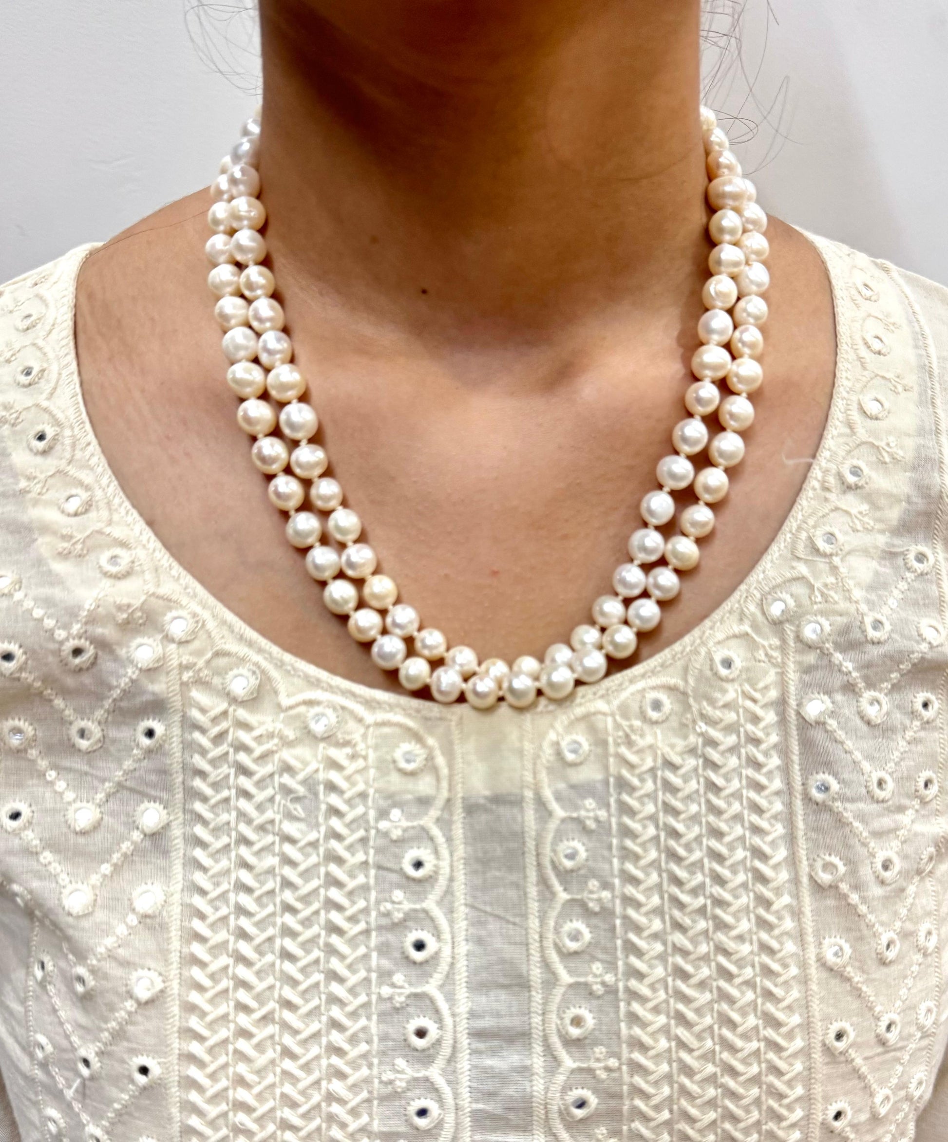 Pearl necklace worn by a person against a neutral background