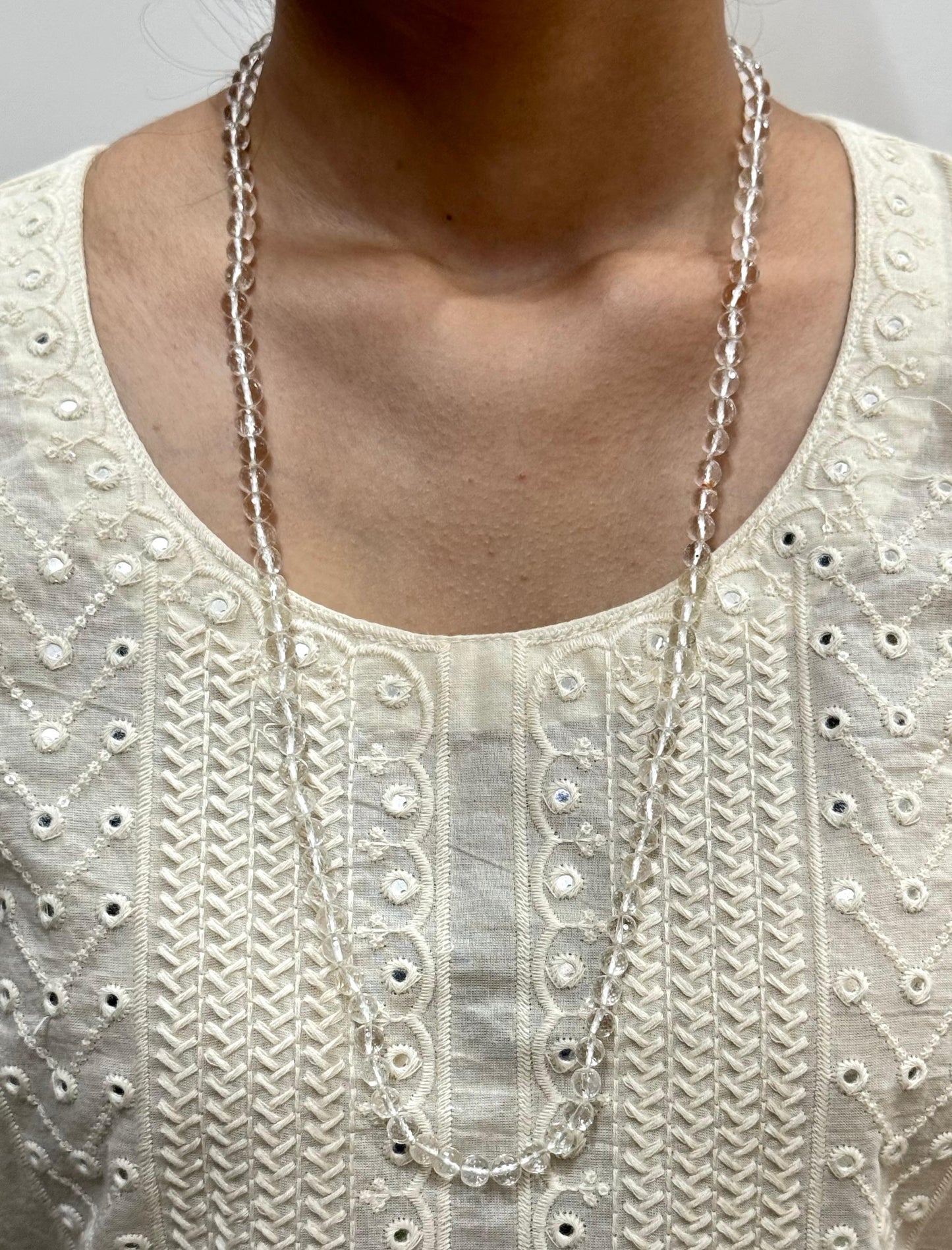 Necklace on a person wearing an embroidered white top
